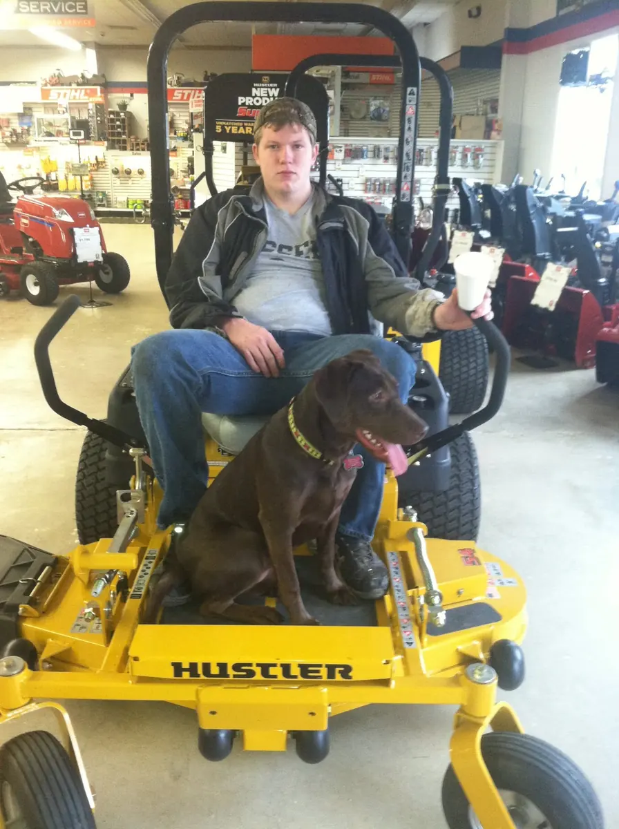 Customer with a chocolate lab on a new Hustler zero-turn mower in the showroom